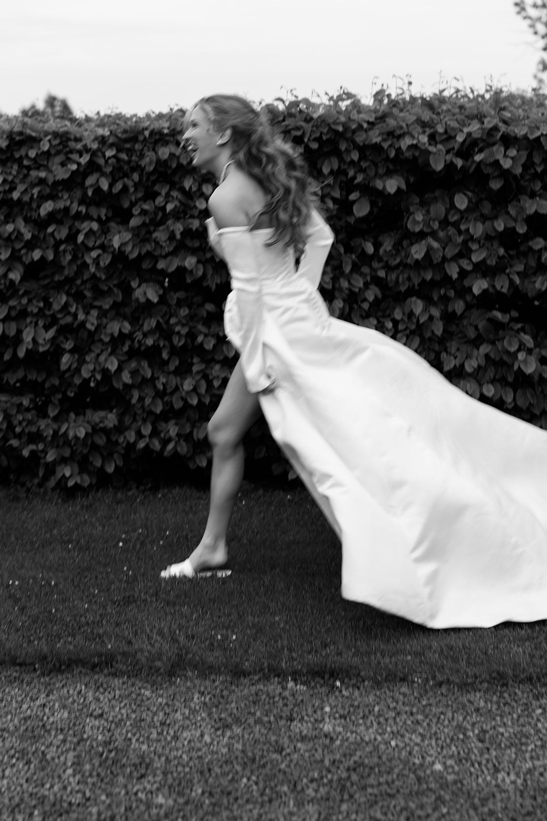 A sequence of black and white photos showing a person in a white dress rolling across grass in front of a hedge.