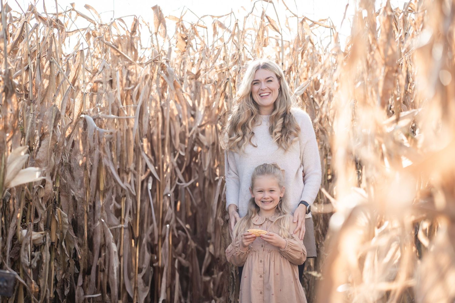 A family stands together in a golden cornfield during autumn as sunlight filters through the dried stalks.