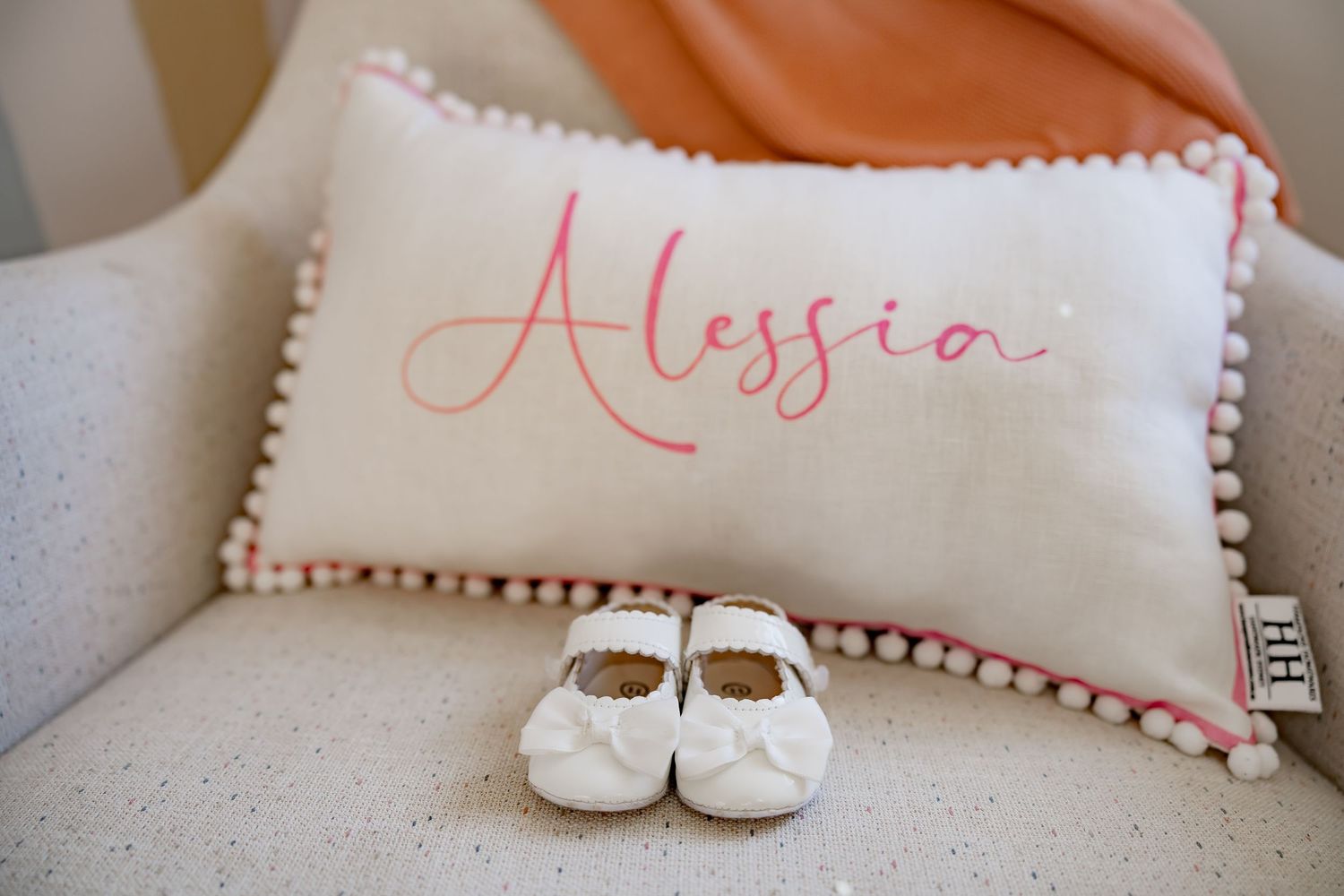 Decorative white pillow with pink pom-pom trim and embroidered text.