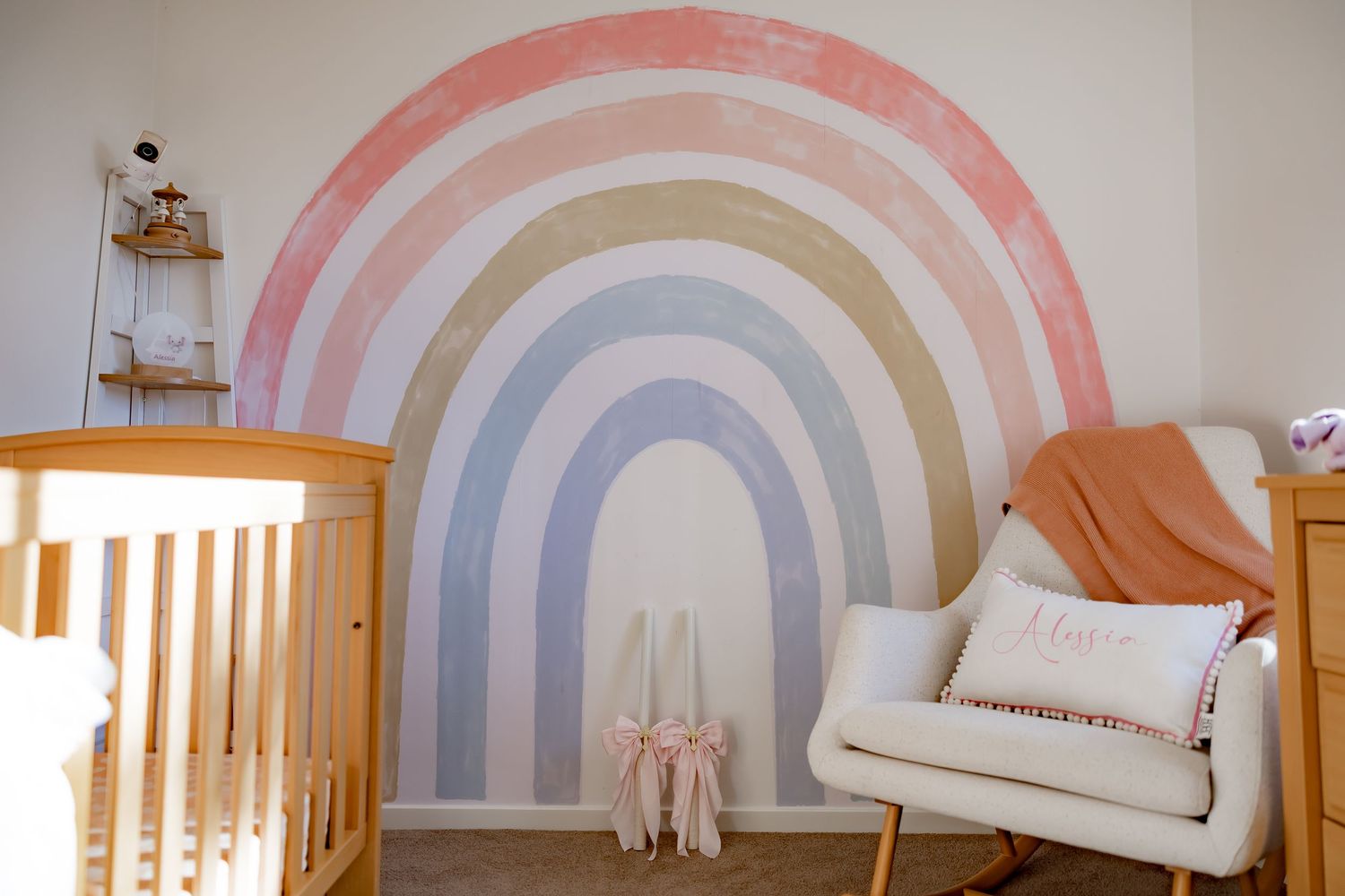 Nursery room with pastel rainbow wall mural and wooden crib furniture.