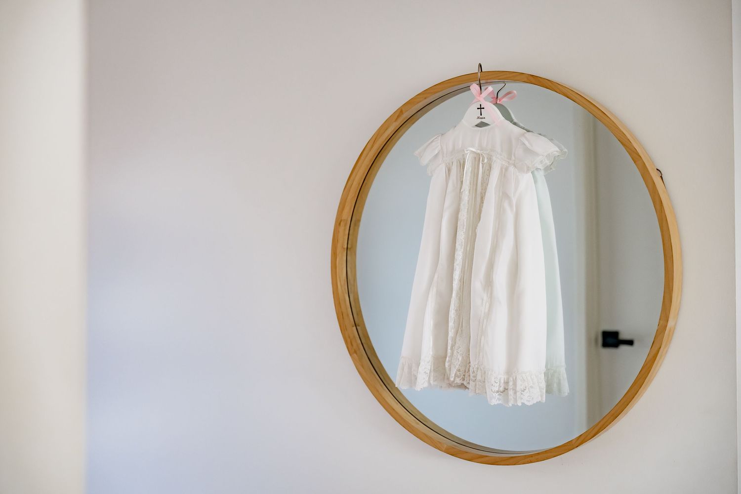 White baby dress displayed in gold circular frame against neutral wall.