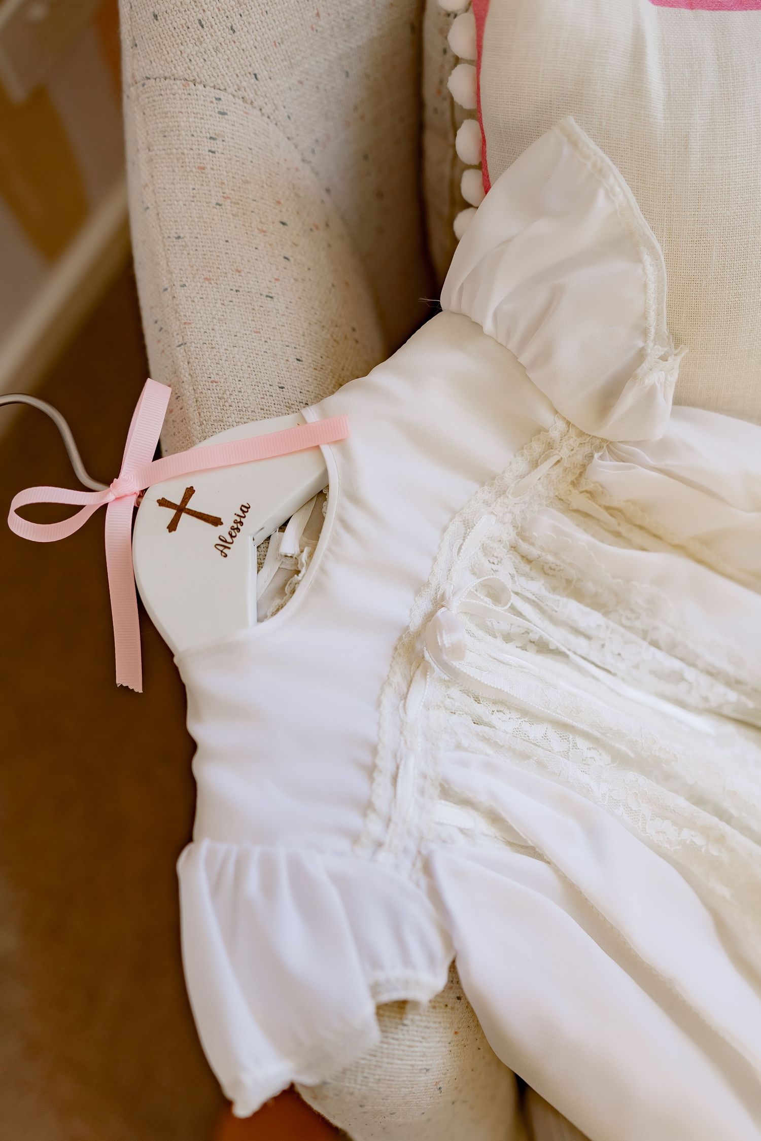 Close-up details of delicate white baptismal gowns with lace trim and pink ribbons.