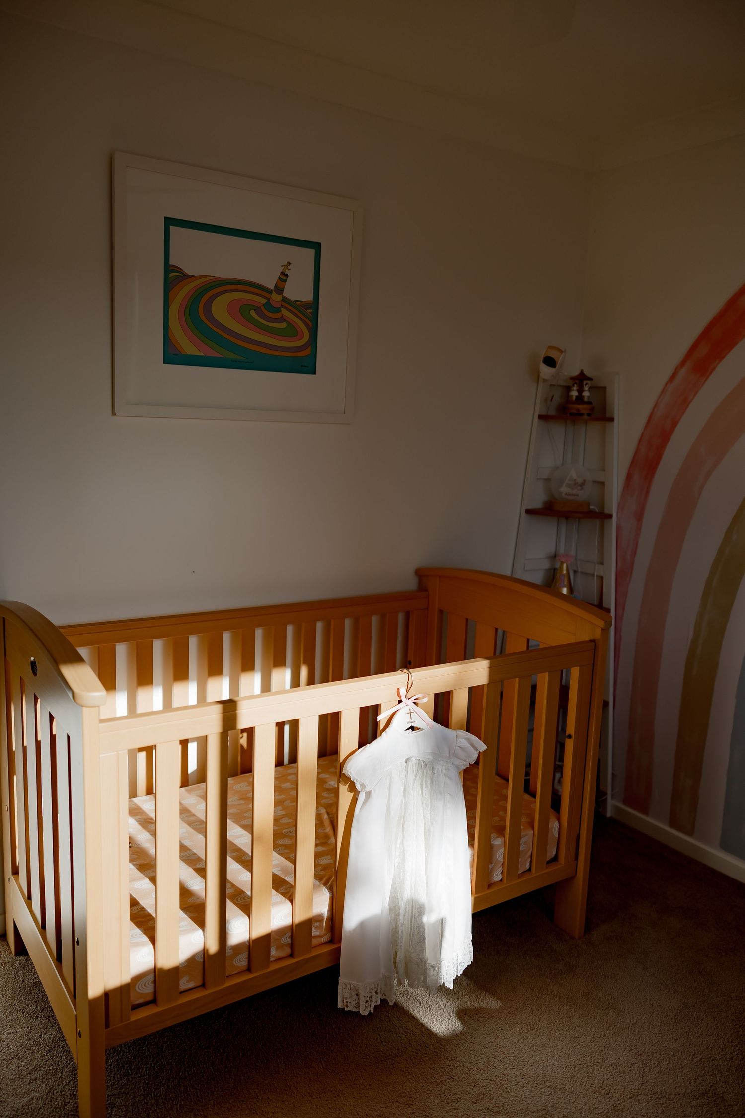 A wooden baby crib with a white christening gown hanging on display in a nursery room.