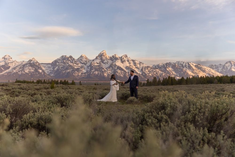 Scenic mountain landscape with snow-capped peaks and sagebrush field during sunset in Grand Teton National Park.