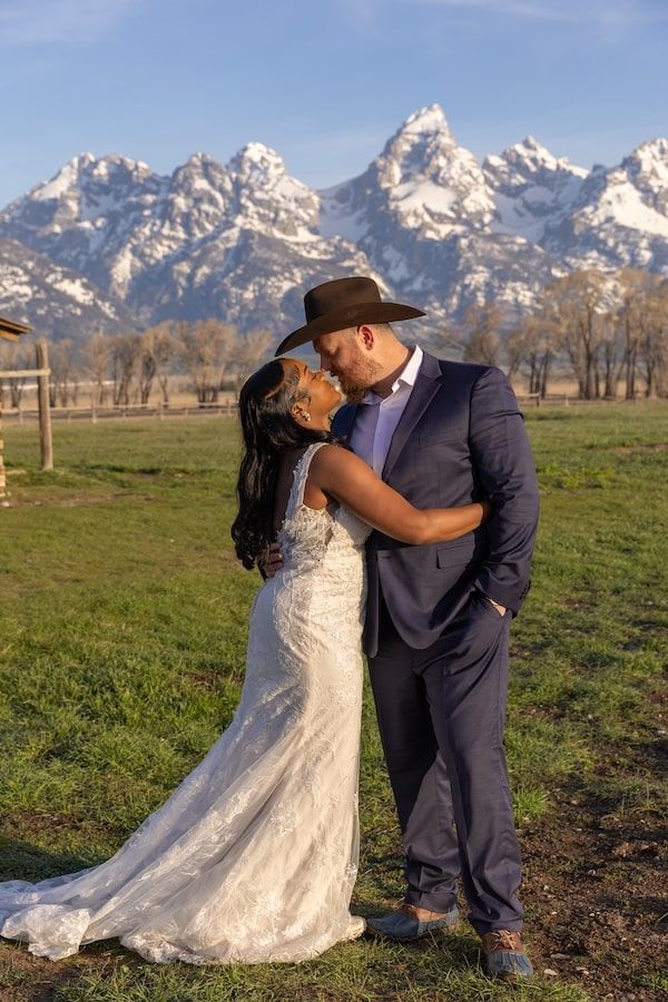A romantic wedding couple shares a tender moment in front of the snow-capped Grand Teton mountains on a sunny day.