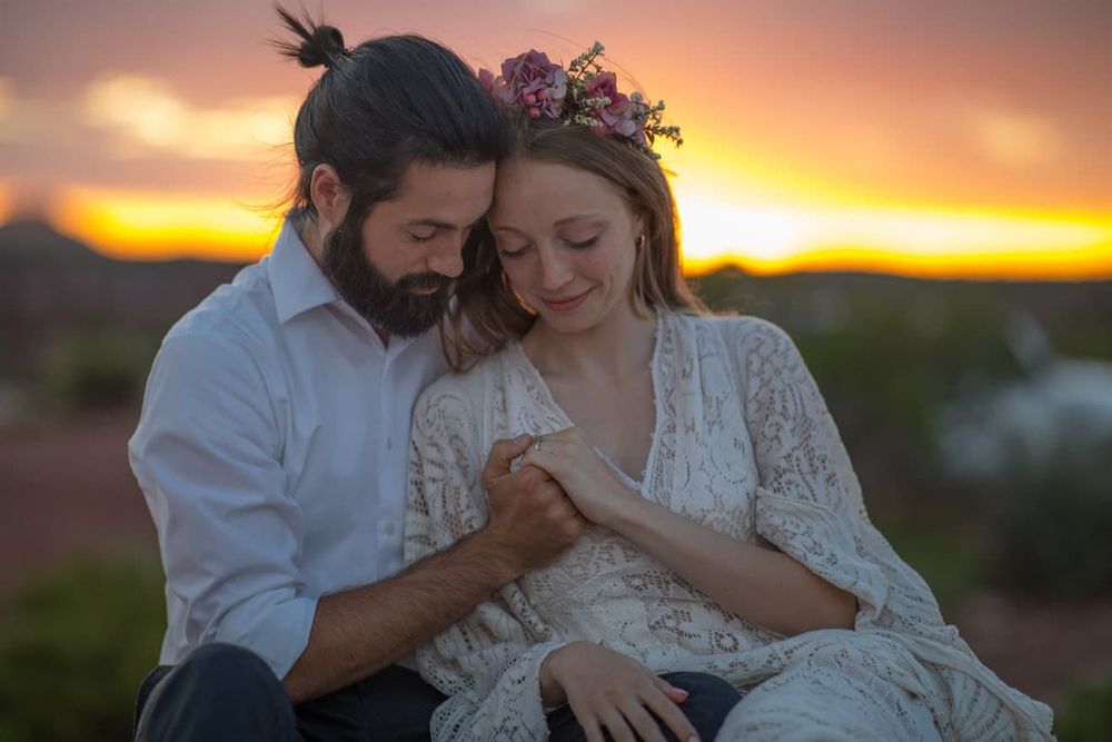 A romantic couple embraces during a golden sunset photoshoot in an outdoor setting.