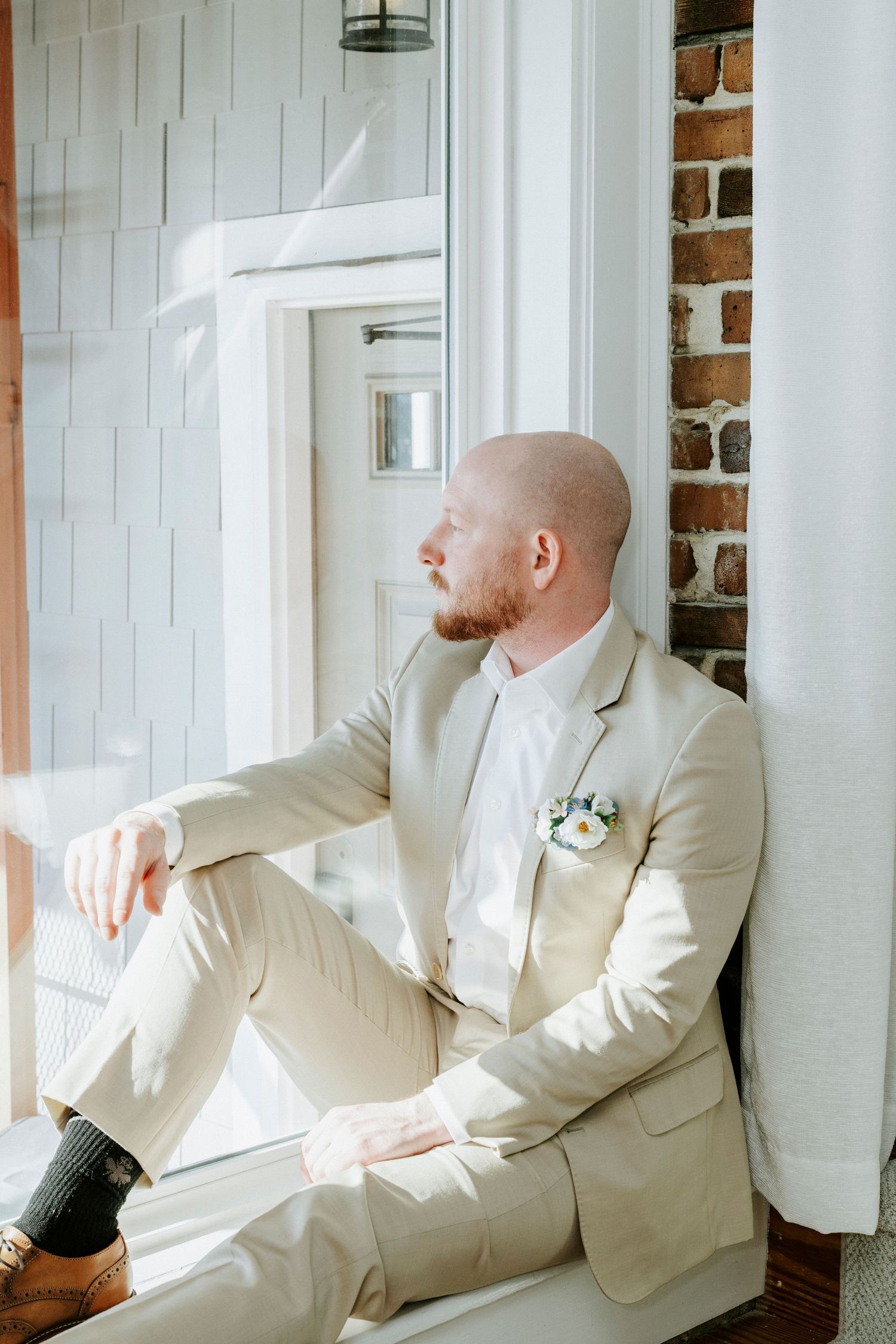 A series of four connected photos showing someone in a cream colored suit sitting by a window with exposed brick walls.
