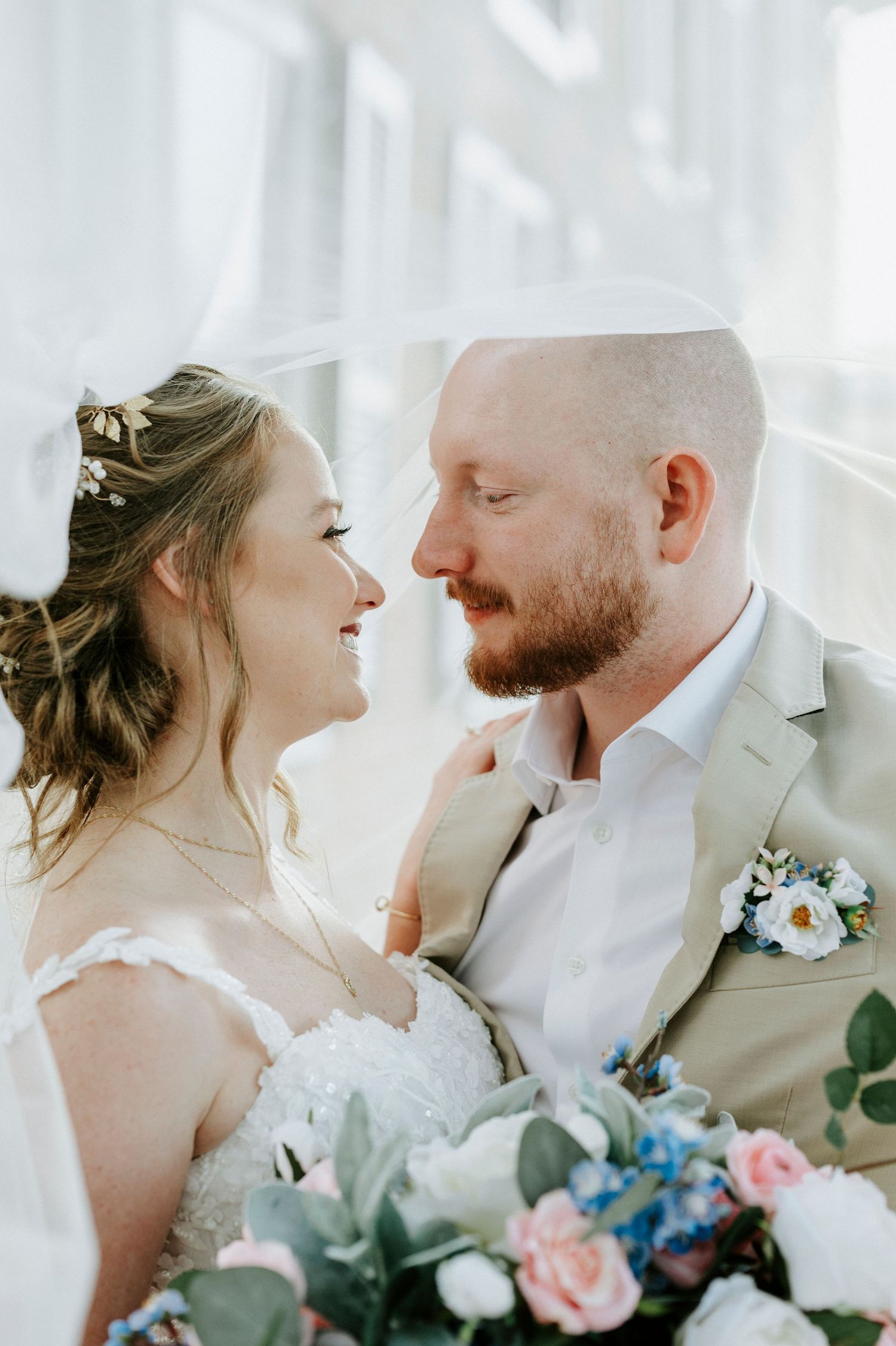A joyful wedding couple shares intimate candid moments while holding floral bouquets in soft natural light.