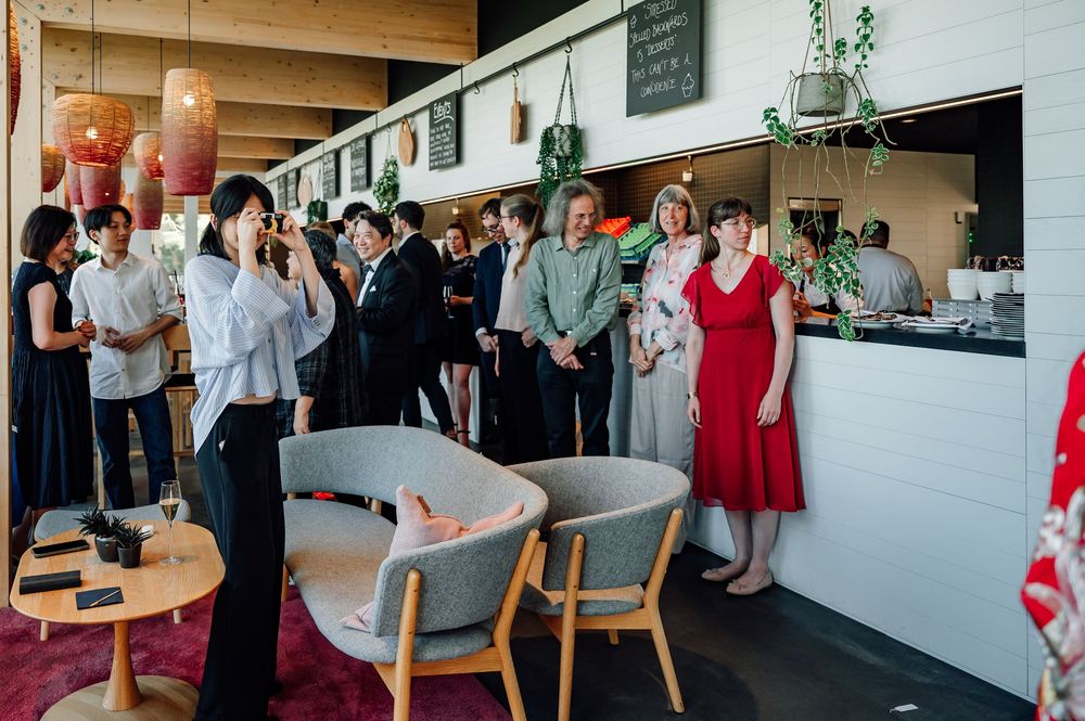 Wedding guests mingle and socialize in a bright reception venue with modern decor and natural lighting.