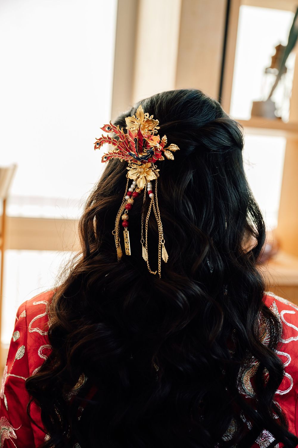 Close-up view of elegant gold and coral floral hair accessories adorning dark curled hair against a bright background.