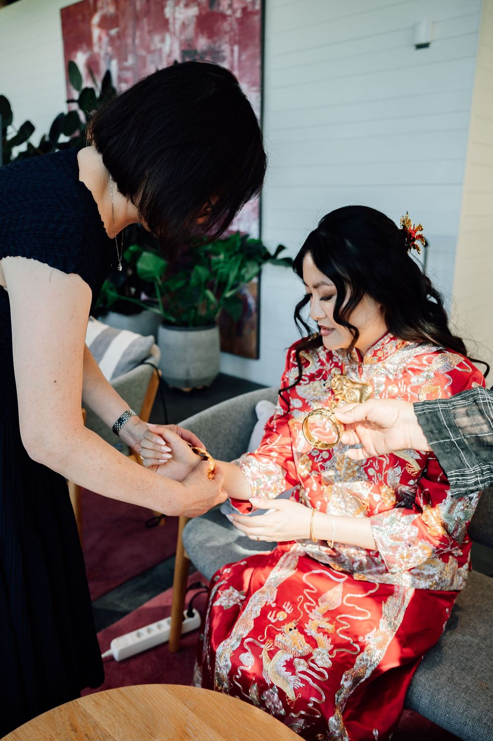 A person wearing a black top assists someone in a vibrant red floral kimono with preparations.