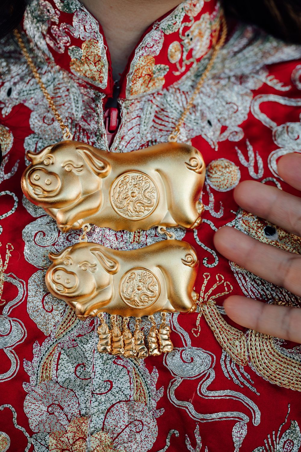 Golden pig ornaments displayed on red and silver traditional Chinese embroidered fabric.