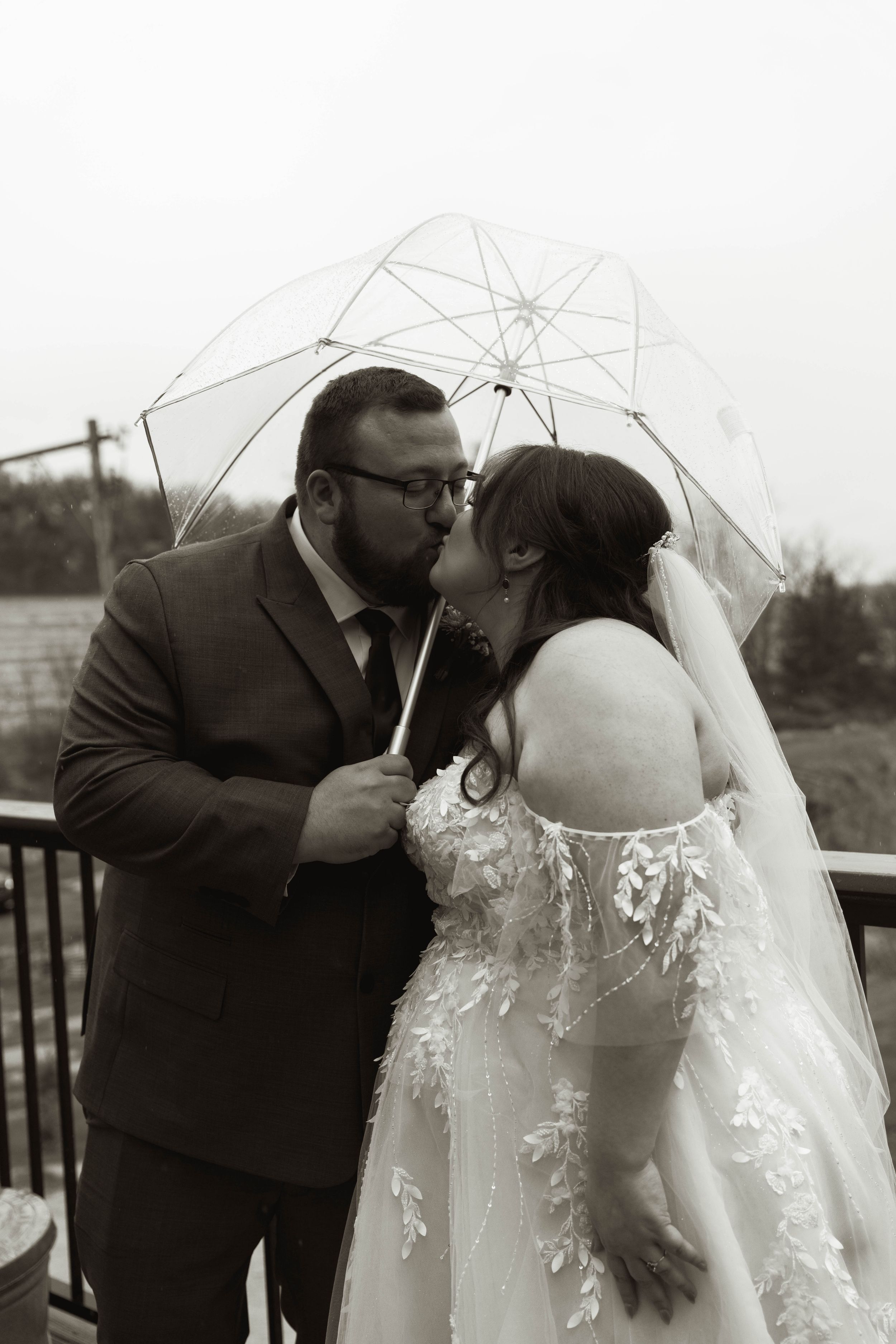 Wedding couple sharing romantic kisses under clear umbrellas on their special day.