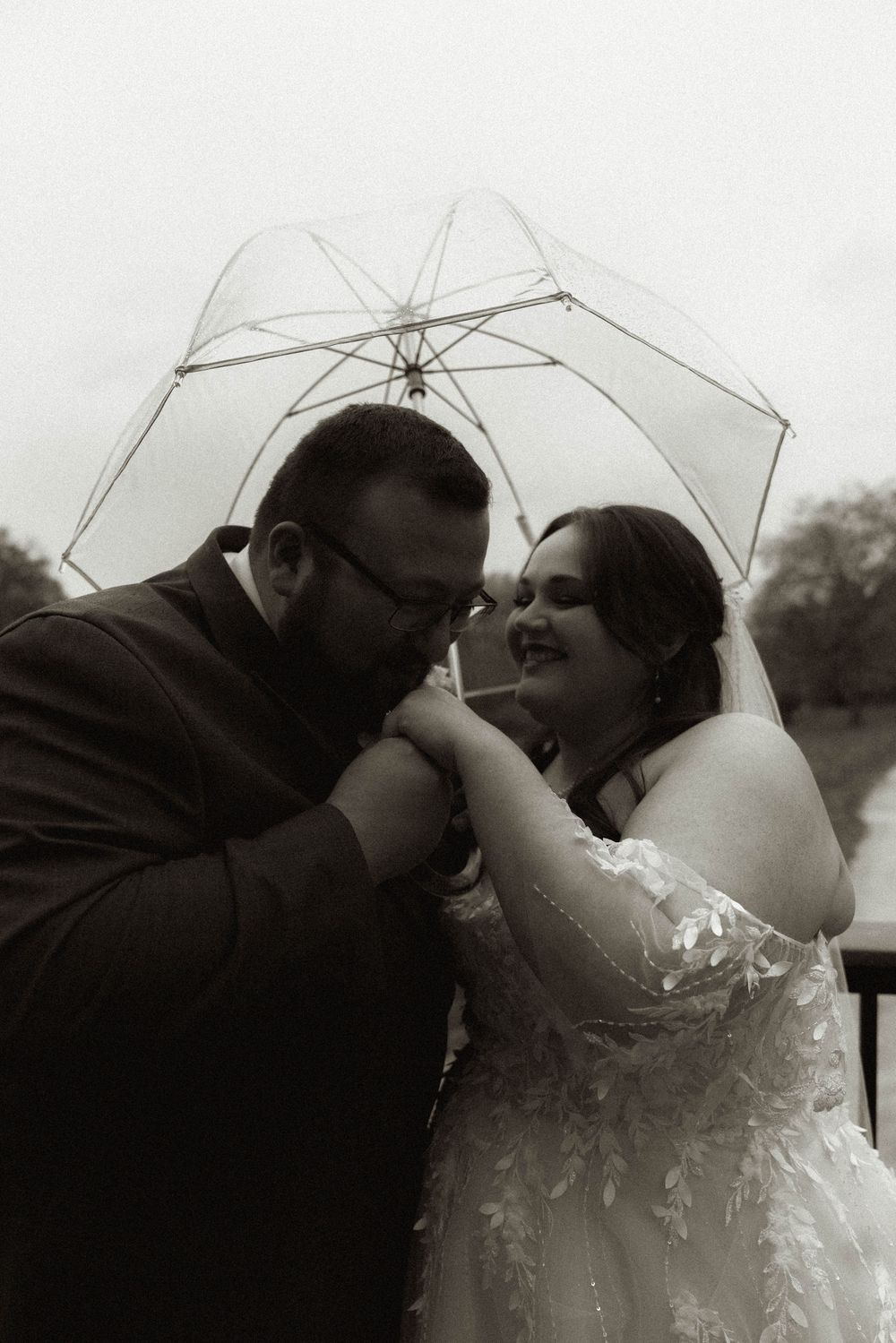 An intimate wedding moment captured under a transparent umbrella in black and white.
