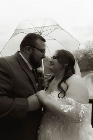 A black and white wedding portrait capturing an intimate moment between newlyweds beneath a clear umbrella.