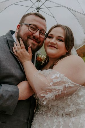 A close-up wedding photo showing a tender moment between newlyweds under a white umbrella.