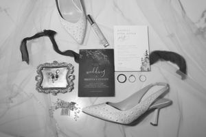 Wedding accessories including sparkly heels, invitation suite, and decorative elements arranged on white fabric.