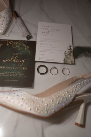 Wedding stationery and sparkly bridal heels arranged with rings for detail photography.