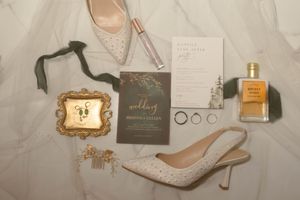 Wedding accessories including perfume bottles, rings, and elegant heels arranged on a marble surface.