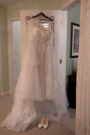 An elegant white wedding dress with lace details hanging on display with shoes beneath.