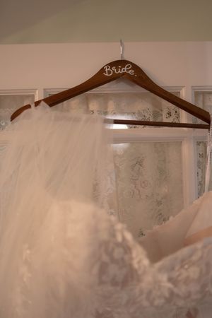 A wooden wedding dress hanger labeled 'Bride' with flowing white tulle veil.