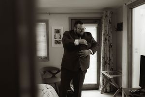 A black and white photograph showing someone adjusting formal attire in a bedroom.