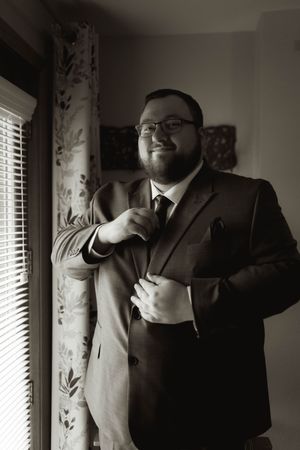 A black and white portrait of someone in formal attire adjusting their suit.