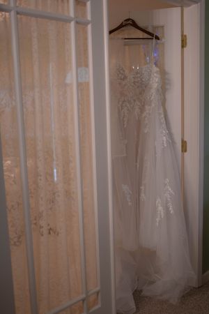 Multiple white wedding dresses displayed on hangers against a curtained wall.