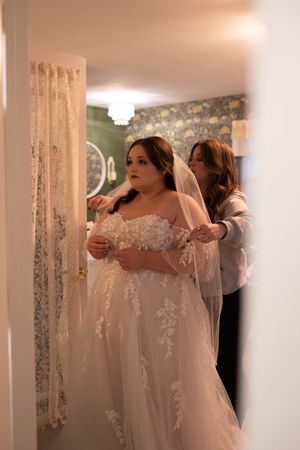 A bride gets assistance with her wedding dress preparations in an elegant room.