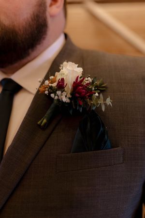 Close-up of boutonnières with burgundy and white flowers on dark suit lapels.