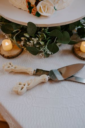 Wedding table decor with eucalyptus leaves, candles, and antique-style serving utensils.