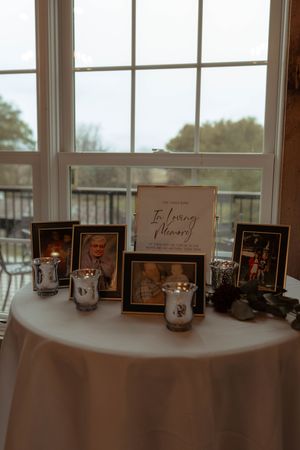 Memorial display table with framed photographs and candles near large windows.