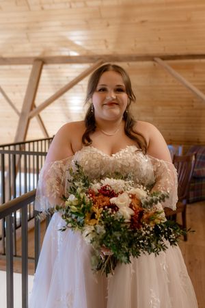 A bridal bouquet with autumn-colored flowers and greenery held against a white wedding dress.