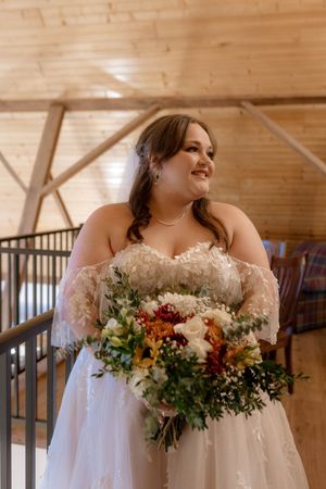 Beautiful wedding bouquet featuring fall colors and mixed florals in a rustic wooden venue.