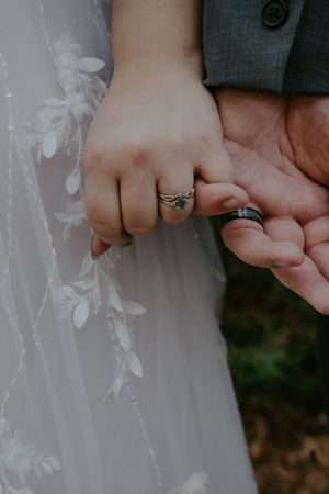 Close-up of wedding rings displayed on hands against white lace dress details.