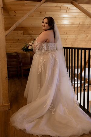 White lace wedding dress with flowing train photographed in a rustic wooden interior.