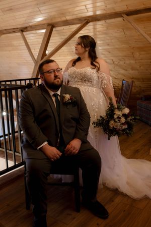 Wedding couple seated in rustic wooden venue with elegant formal attire.