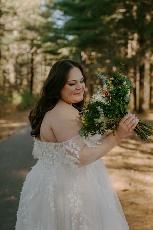 Bride with floral bouquet poses in sunlit forest setting.