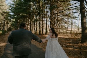 Couple walking hand in hand down a pine-lined forest path.
