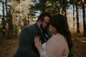 Romantic couple embraces during outdoor wedding photoshoot among pine trees.