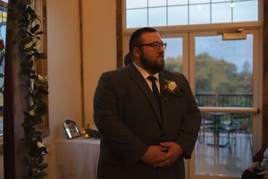 Wedding party members standing in a rustic venue with large windows and natural light.