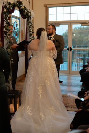 A flowing white wedding dress with delicate lace details and a long train displayed in a sunlit venue.