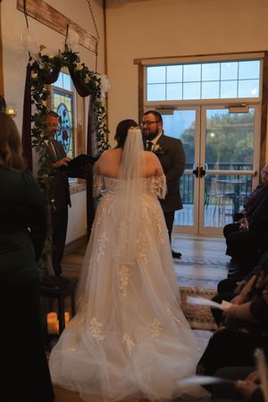 A wedding ceremony under a floral arch with guests watching the couple exchange vows.