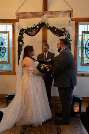 Wedding ceremony taking place in an intimate wooden-beamed venue with stained glass windows.