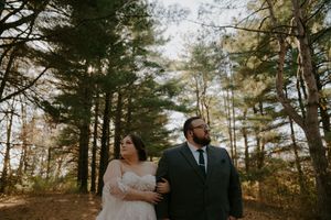 Wedding couple poses against backdrop of tall pine trees in natural setting.