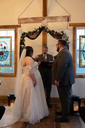 Wedding ceremony proceedings in a rustic venue with decorative greenery and wooden beams.
