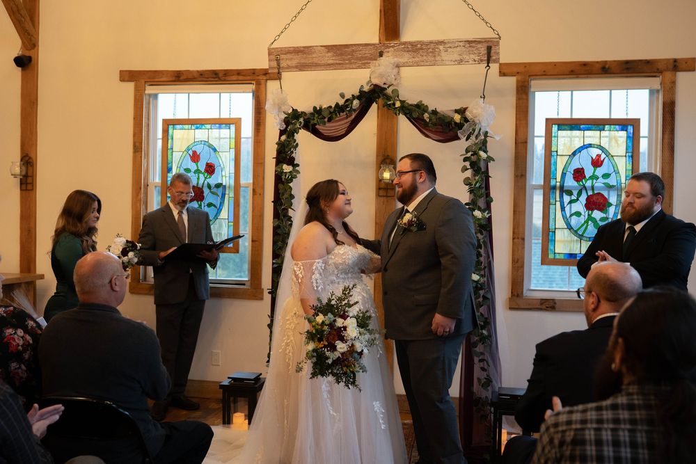 A wedding ceremony taking place in a rustic chapel with stained glass windows and wooden beams.