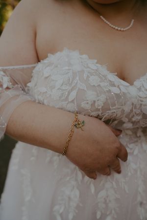 Close-up of delicate lace wedding dress bodice with pearl necklace and gold charm bracelet.