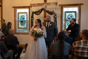 Wedding ceremony in a chapel with stained glass windows and rustic wooden arch.
