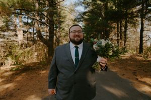 Outdoor portrait in a wooded setting wearing a formal dark suit and holding flowers.